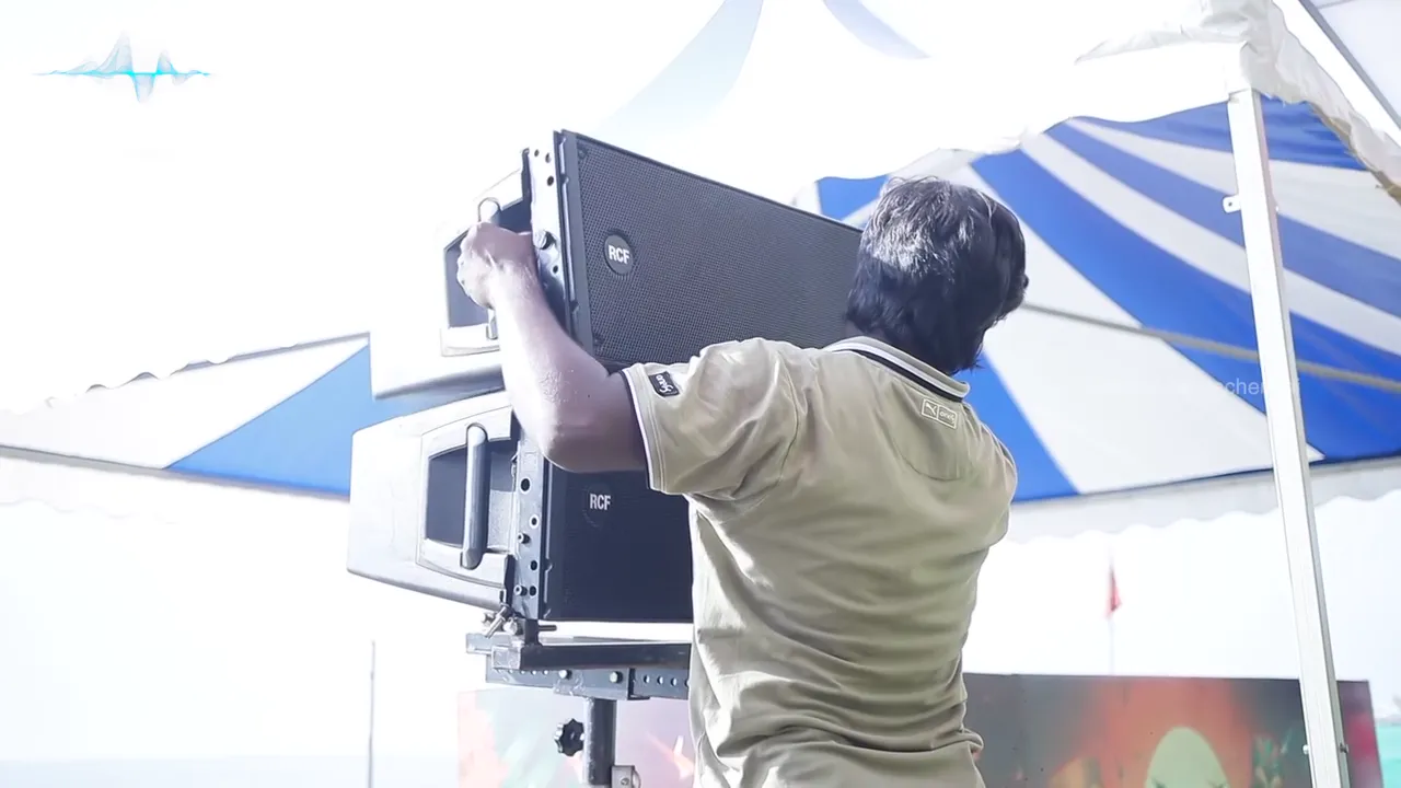 Crew mounting a speaker on a stand under the tent